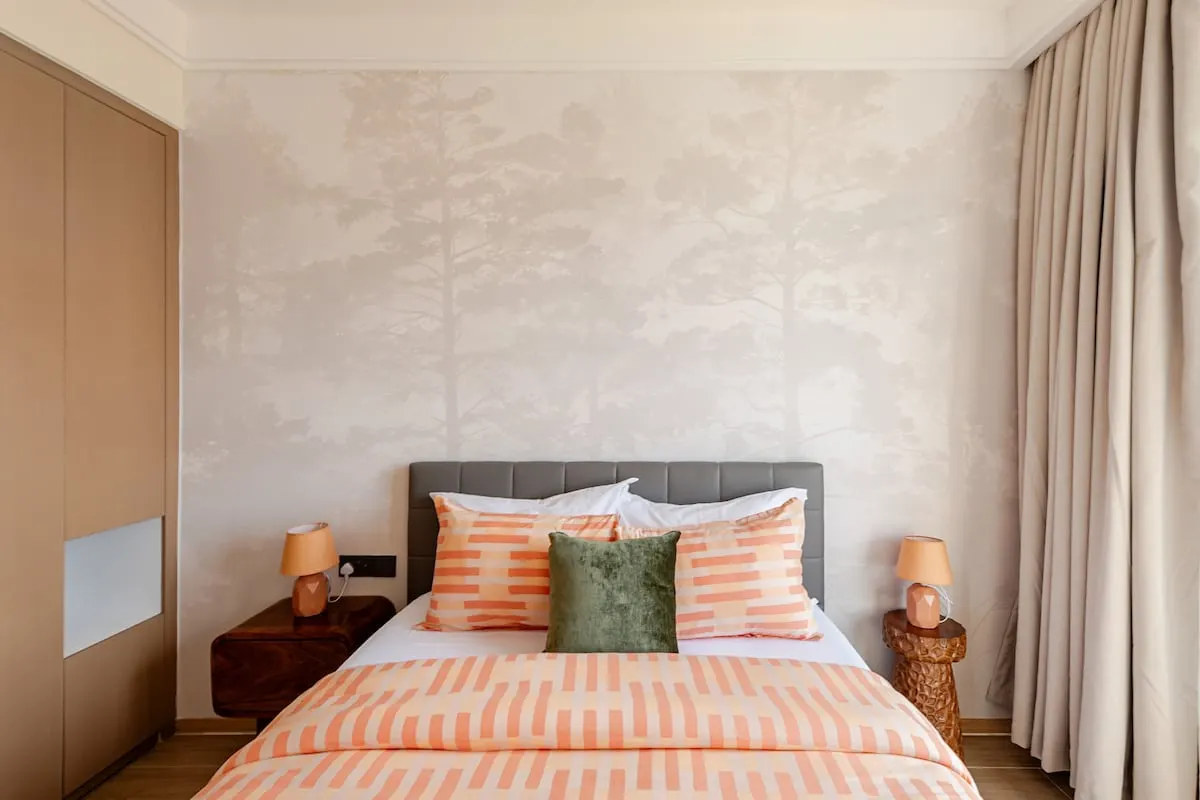 Queen bed made up with orange patterned bedding and two bedside lamps
