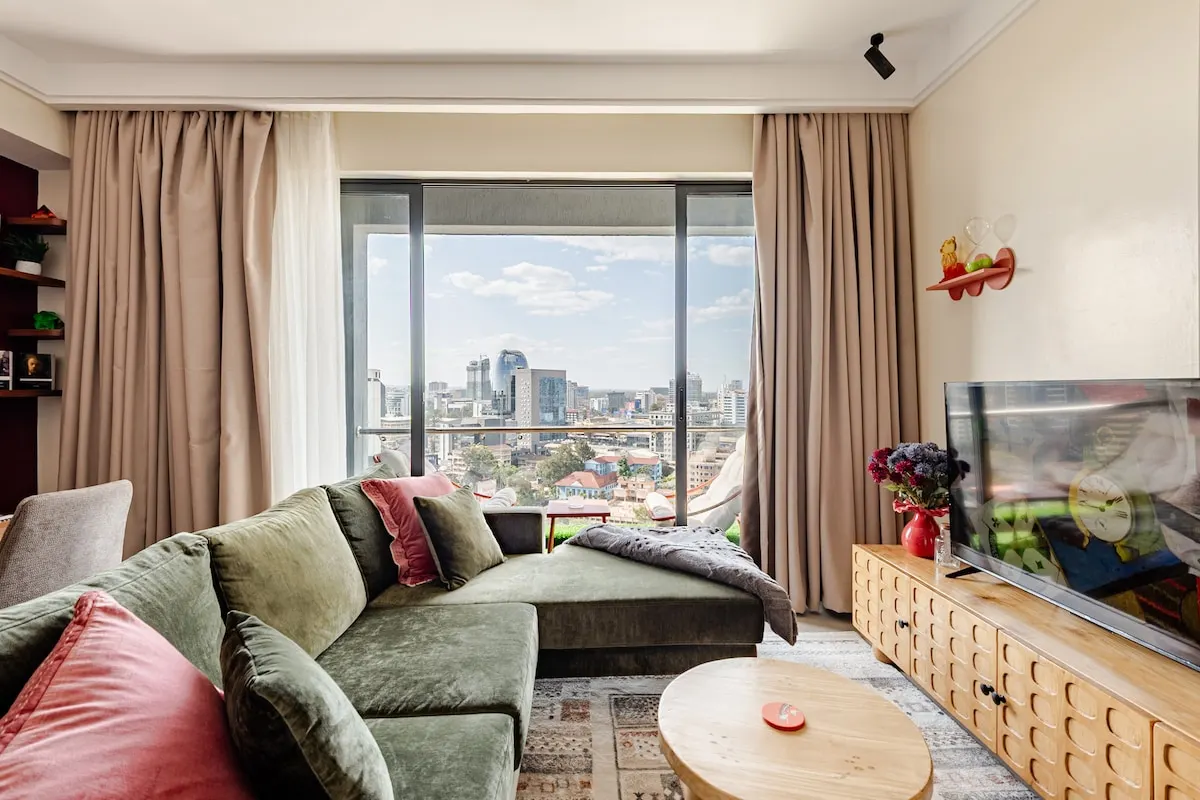 Living room with a green velvet sofa and floor-to-ceiling windows over the city